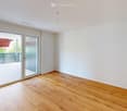 Empty room with wooden flooring, white walls, and large sliding glass doors leading to a balcony or terrace.