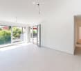Empty room with white tiled floor, white walls, large sliding glass doors leading to outdoor area, and a hallway leading to another room.