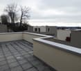 Balcony / Terrace. Roof terrace with tiled flooring, low white parapet walls, and surrounding buildings visible in the background.