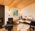 Modern living room with exposed wooden ceiling, fireplace, white sofa, black leather chair, and wooden floor.