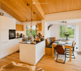 Open-plan kitchen and dining area with white cabinets, wooden ceiling, pendant lights, and a dining table with chairs.