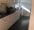 Modern kitchen with white cabinets, black tiled floor, and black countertops. Features a sink, dishwasher, and various kitchen utensils on the counter.