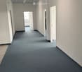 Empty hallway with grey carpeted floor, white walls, and several doors leading to adjacent rooms.