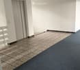 Clean, modern hallway with white walls, tiled floor, and carpeted area. Features a white door frame and a small white railing on the left side.