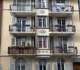 4 story building, beige paint, white shutters, balconies, windows, metal railings, potted plants