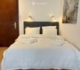 Cozy bedroom with a neatly made double bed, white bedding, two wall-mounted lamps, and a large mirror on the wall.