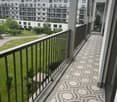 Balcony with decorative tile flooring, metal railing, and a view of a green park and modern apartment buildings.
