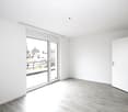 Empty room with white walls, light wooden flooring, and a large sliding glass door leading to a balcony.