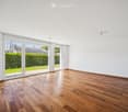 Empty room with wooden flooring, white walls, and large sliding glass doors leading to a green outdoor area.