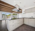 Modern kitchen with white cabinets, stainless steel range hood, and a black countertop, featuring large windows with a scenic view.