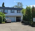 Two-story modern house with a flat roof, large windows, garage, and driveway with a parked car.