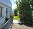 Balcony area with a view of a well-maintained garden, featuring a variety of flowering plants and trees, leading to a grassy lawn and distant landscape.