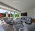 Modern living room with large windows, grey sofa, coffee table, chairs, and television.