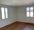 Empty room with wooden flooring, white walls, and two windows with white frames. A white radiator is visible on one wall.