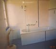 Bathroom with a bathtub, tiled walls, a window, and a handrail for safety.