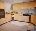 A modern kitchen with light wooden cabinets, a stainless steel oven, a dishwasher, and various kitchen items on the counter.
