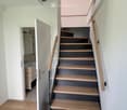 Modern staircase with wooden steps and a glass railing, leading to a bathroom with a sink and mirror.