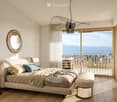 Modern bedroom with a large bed, nightstands, a round mirror, and a view of the sea through large windows and a balcony.