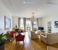 Elegant living room with wooden flooring, large windows offering a view, a fireplace, a chandelier, a sofa, armchairs, coffee table, and decorative plants.