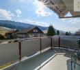 Balcony with a modern railing, overlooking a scenic countryside with houses and mountains in the background.