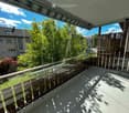 Modern balcony with glass railing, wooden balusters, and a view of a green garden and neighboring house.