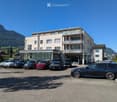 3 story building with many windows, balcony, outdoor parking lot, surrounded by mountains