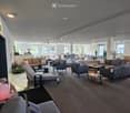 Furnished Room. Modern, spacious living room with multiple seating areas, including sofas, chairs, coffee tables, and decorative lamps. Large windows allow natural light to fill the space.