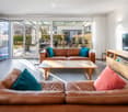 Bright living room with large glass doors leading to a patio, leather sofas, a coffee table, a TV stand, and a bookshelf.