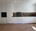 Modern kitchen with white cabinets, stainless steel sink, oven, and wooden flooring.