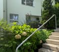 white painted house, raised ground floor, stairs leading to entrance, garden with shrubs and flowers