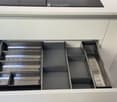Modern kitchen cabinet with multiple open drawers and compartments, featuring sleek white surfaces and stainless steel accents.
