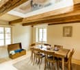 Bright dining area with wooden dining table and chairs, wooden chest with flowers, floor lamp, and candle on windowsill.