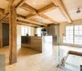 Modern kitchen with exposed wooden beams, stainless steel appliances, and a central island. Large windows provide natural light.