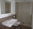 Modern bathroom with a white sink, chrome faucet, toilet, and a large mirror above the sink. The walls are tiled in neutral tones, and the floor is covered with light brown tiles.