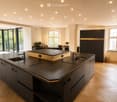 Modern kitchen with dark countertops, island, sink, and cabinets. Large windows and a balcony are visible.