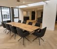 Modern, open-plan office space with a large wooden conference table surrounded by black chairs, large windows with a view of greenery, and a sleek, contemporary design.