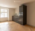 Modern kitchen with grey cabinets, a sink, a faucet, and an oven, featuring wooden flooring and a large window.