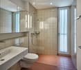 Modern bathroom with beige tiled walls, a white sink with a chrome faucet, a toilet, a large mirror, and a glass-enclosed shower area.