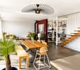 Modern open-plan living and dining area with a wooden dining table, chairs, bench, shelves, and decorative plants.