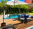Outdoor patio area with a swimming pool, a dining table with chairs, and a large umbrella providing shade. There is a decorative swan float in the pool and a potted plant nearby.