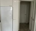A modern kitchen with white cabinets and a large refrigerator, leading to a tiled hallway with doors.
