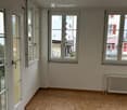 Empty room with wooden flooring, large windows, and a radiator on the wall.