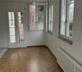 Empty room with wooden herringbone flooring, white walls, large windows, and a radiator. No furniture or equipment present.