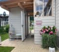 A cozy outdoor area with a brick pathway leading to a house entrance, featuring a small table, a birdcage with flowers, potted plants, and decorative signs on the wall.