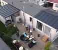 Aerial view of a modern house with a patio area, outdoor furniture, and a small garden. The patio includes a dining table, chairs, and a grill, surrounded by greenery and neighboring houses.