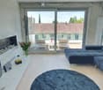 Modern living room with a dark blue sectional sofa, a white coffee table, a fireplace, a large window offering a view of the city, and a small outdoor seating area visible through the glass doors.