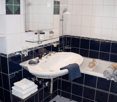 Bathroom. Modern bathroom with white tiles, dark blue lower tiles, a sink, bathtub, and neatly arranged towels and toiletries.
