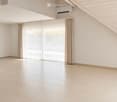 Empty room with light-colored tiled flooring, white walls, large window with beige curtains, and an air conditioning unit mounted on the wall.