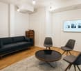 Modern living room with a dark blue sofa, glass coffee table, three grey chairs, a large screen displaying images, and a wooden cabinet.