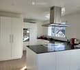 Modern kitchen with white cabinets, black countertop, stainless steel appliances, and a large window offering a view.